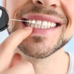 The image shows a close-up of a smiling person's lower face, highlighting their teeth. A finger is pointing to one of the teeth, and there is an inset graphic of a dental implant next to the area being pointed at.